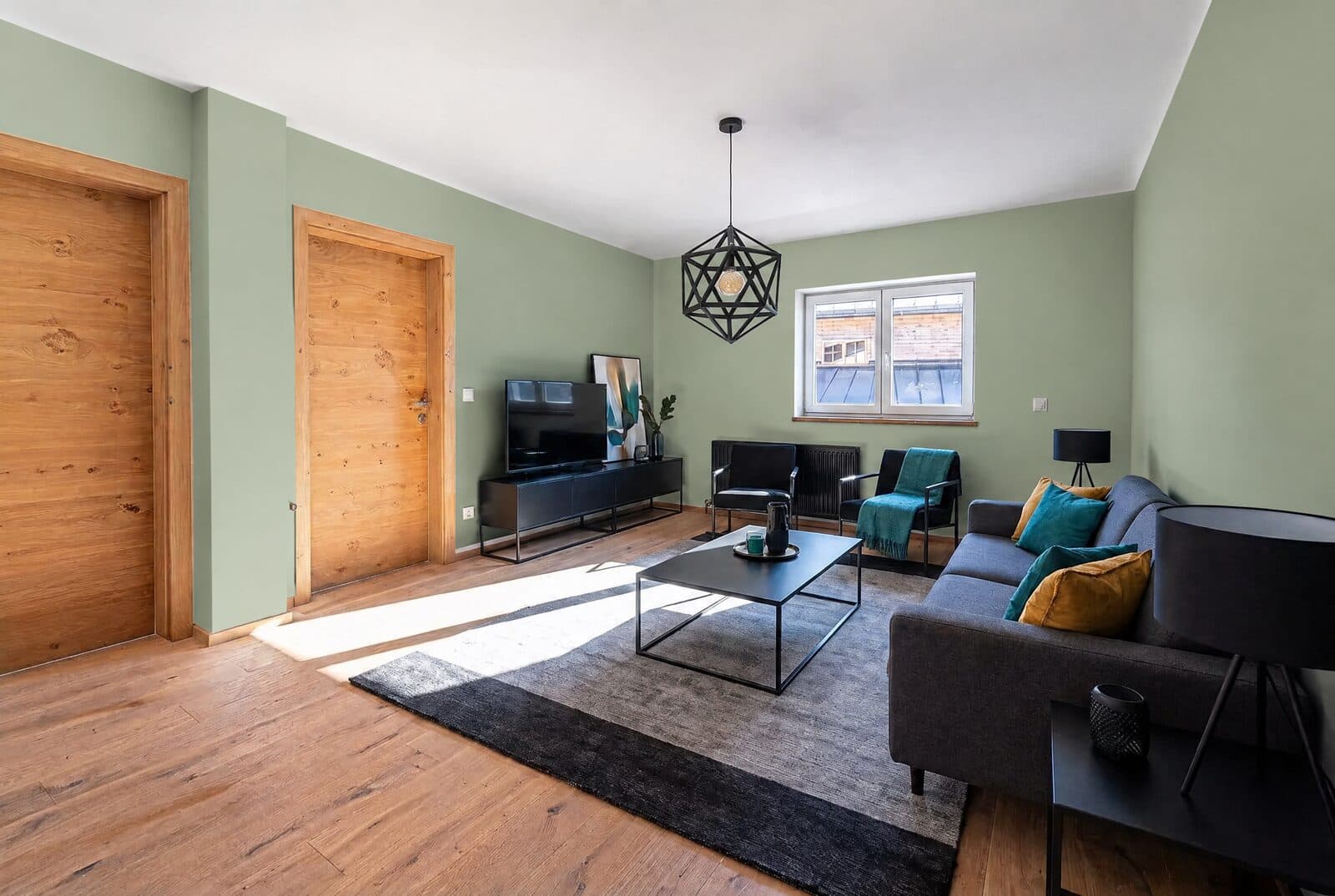 Helles Wohnzimmer mit Holztüren und dunklem Sofa, Wände in Salbeigrün
